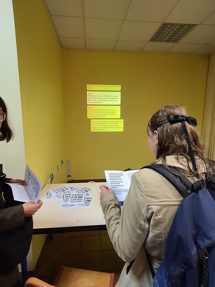 © Angeliki Monnier, photo du vernissage de l'exposition « La retraite à 20 ans et des frites tous les jours » de Thomas Tudoux à la galerie Essais Dynamiques : visiteurs lisant le texte sur le méritat