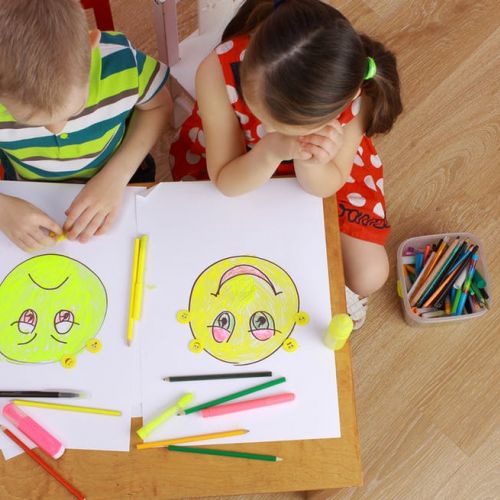 Deux enfants dessinent chacun sur une feuille de papier un tête d'enfant type smiley